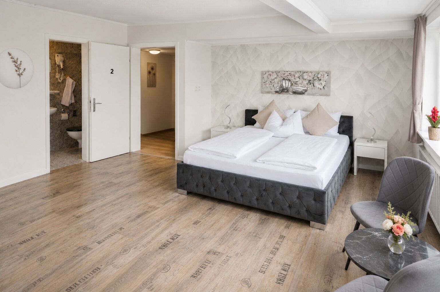 Une chambre à coucher avec un lit, des tables de chevet, une chaise et une petite table sur laquelle est posé un vase.