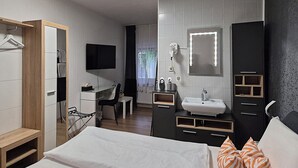 A modern hotel room with a bed, a desk, a mirror, a wardrobe, and a bathroom with a sink and mirror. - Schloßschenke (Idar-Oberstein)