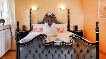 A four-poster bed with a tufted headboard, two bedside tables, and decorative wall sconces.
