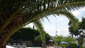 A pool area with lounge chairs and umbrellas, surrounded by palm trees and a stone wall. - Residence La Carruba (Diano Marina)