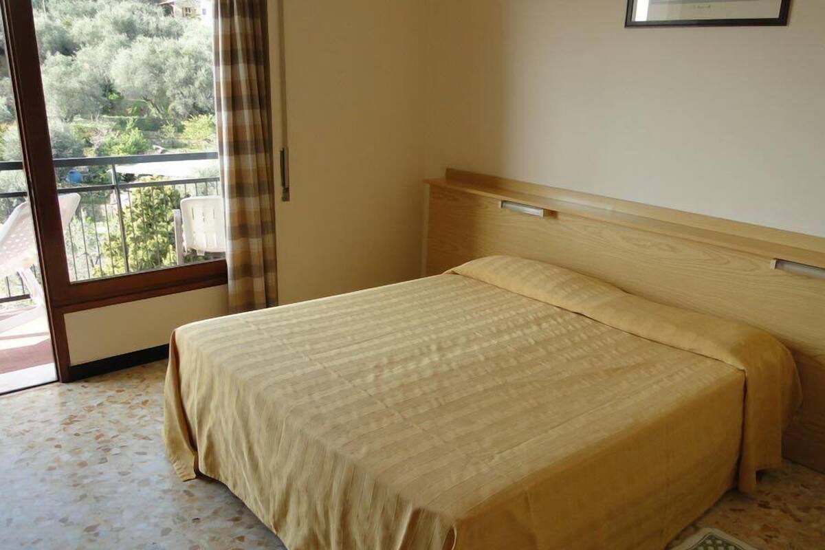 Une chambre d’hôtel avec un lit, une fenêtre donnant sur un espace verdoyant et une porte menant à un espace extérieur.
