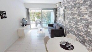 A modern living room with a white tiled floor, a round dining table with wine glasses, a grey sofa, and a brick-patterned wall. - Modern 2P apartment with terrace in Menton (Menton)