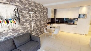 A modern living room with a gray sofa, a dining area with white chairs, and a kitchen with white cabinets and a black countertop. - Modern 2P apartment with terrace in Menton (Menton)