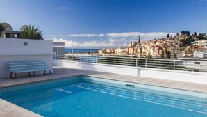 A rooftop swimming pool with a bench, a view of a coastal town, and a clear sky. - Modern 2P apartment with terrace in Menton (Menton)