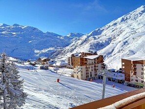 A snow-covered mountain town with ski slopes, wooden buildings, and a clear blue sky.