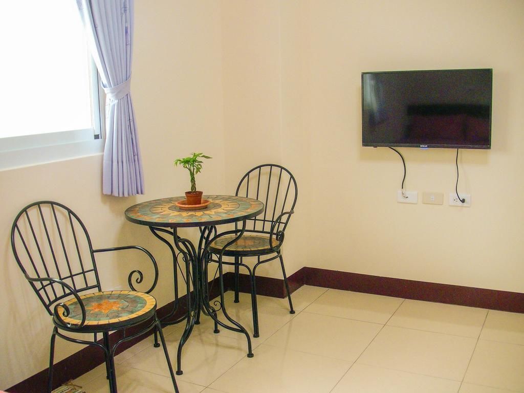 A small dining area with a round table and four chairs, a potted plant, and a flat-screen TV mounted on the wall.