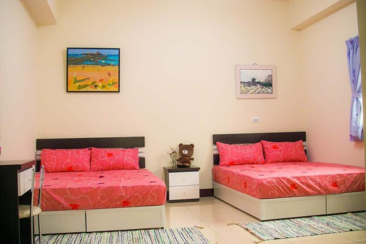 A bedroom with two beds, a nightstand, a teddy bear, and two framed pictures on the wall.