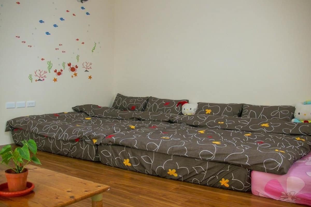 A room with a sofa bed, a small table with a plant, and a wall decoration of fish and seaweed.