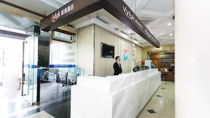 A hotel reception area with a marble counter, a television mounted on the wall, and a sign with the hotel name.