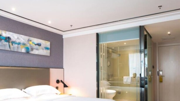 A modern hotel room with a large bed, a glass shower enclosure, and a painting on the wall.