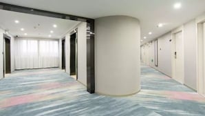 A hotel corridor with a patterned carpet, a large pillar, and doors leading to rooms.