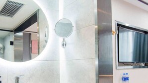 A modern bathroom with a rectangular sink, a round mirror, and a flat-screen TV mounted on the wall.