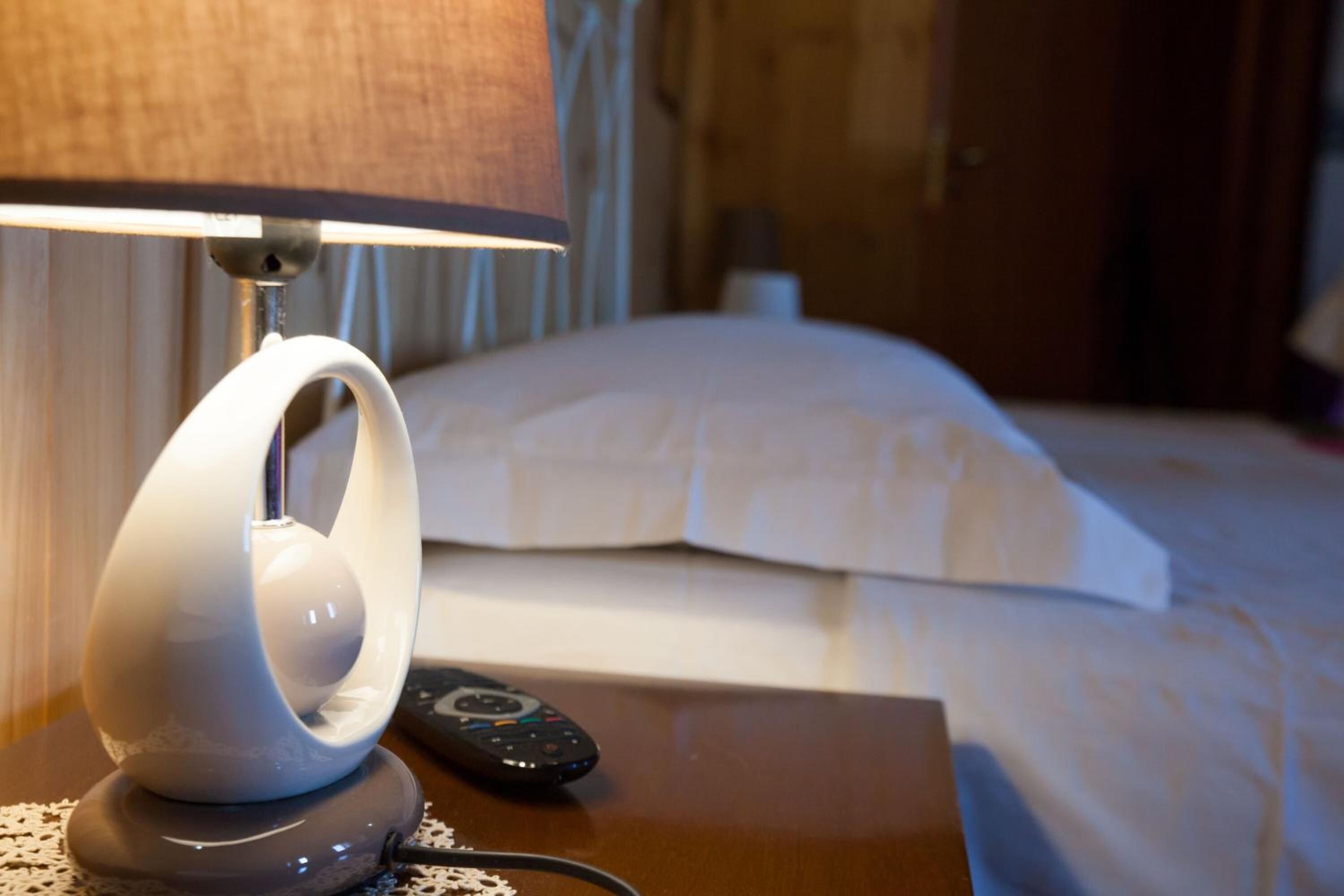 Un lit avec une literie blanche, une télécommande et une lampe sur une table de chevet.