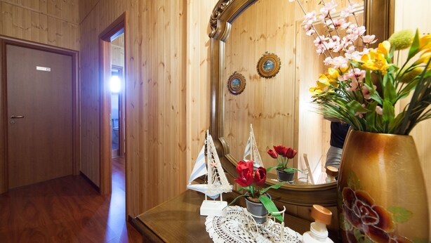 A wooden-paneled hallway with a wooden door, a small table with a decorative sailboat, a vase with flowers, and a mirror reflecting the room. - Acqua Di Mare (Misiliscemi)