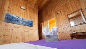 A wooden cabin room with a bed, a painting, a mirror, and a bathroom door. - Acqua Di Mare (Misiliscemi)
