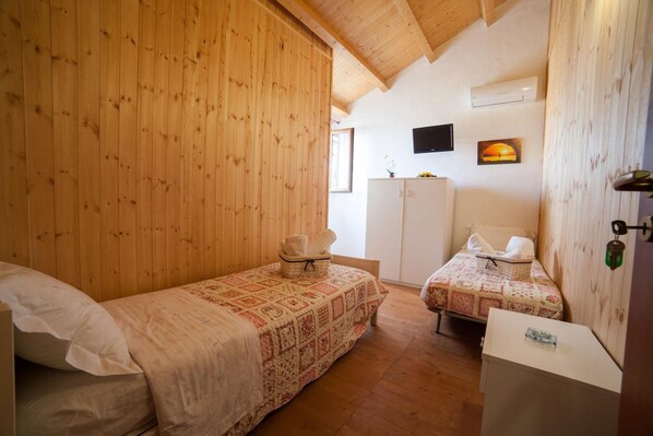 Una habitación acogedora con dos camas individuales, paredes de madera, un televisor de pantalla plana y un mueble pequeño.