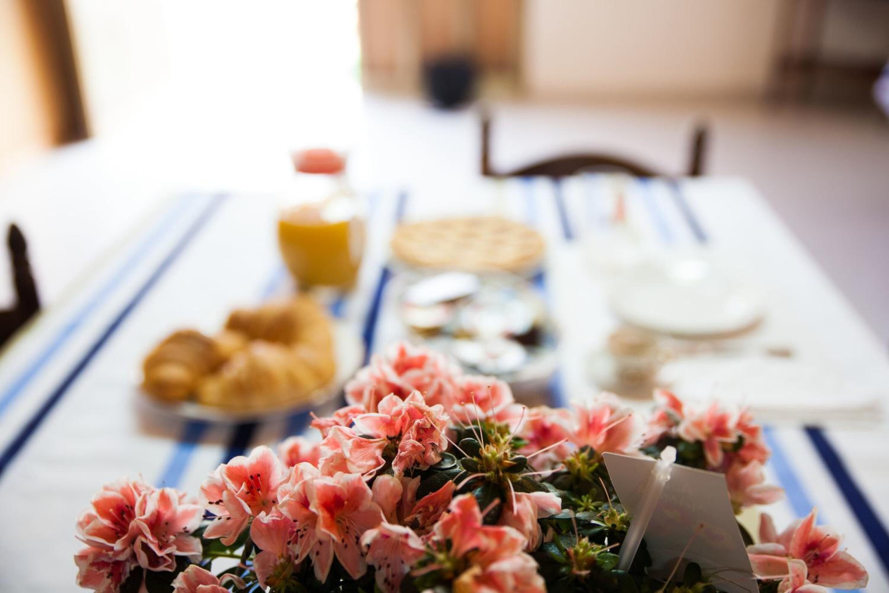Une table à manger agrémentée d’un centre de table floral, une bouteille de jus d’orange et une assiette de pâtisseries.