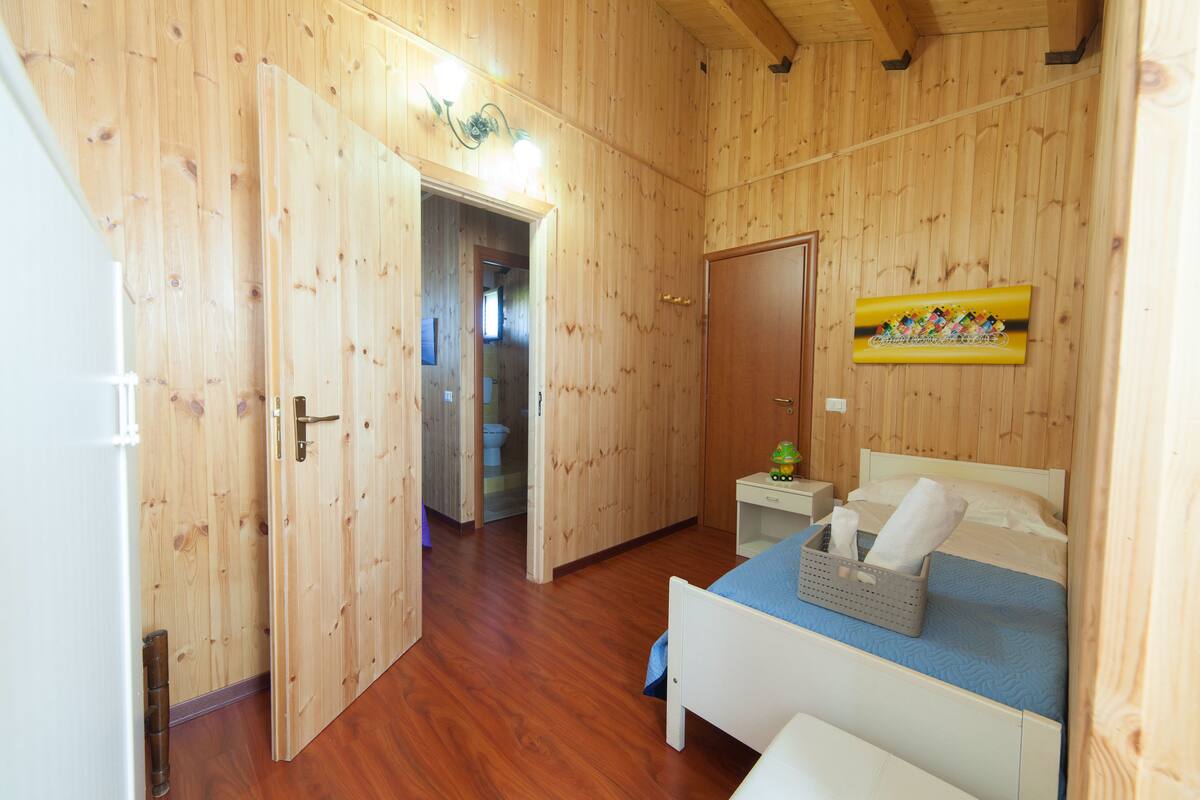 A wooden-paneled room with a bed, a nightstand, and a door leading to a bathroom.