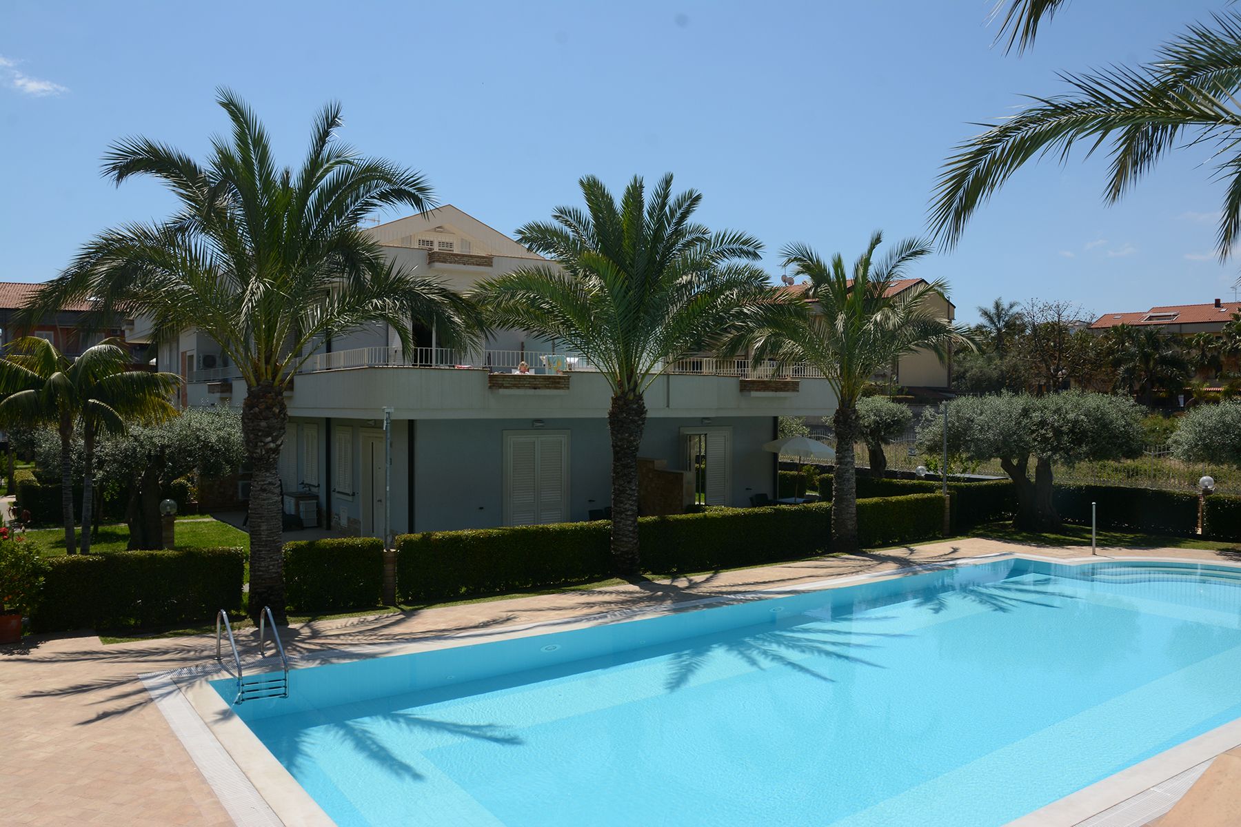 Ein Swimmingpool mit klarem, blauem Wasser, umgeben von Palmen und einem Gebäude mit einem Balkon.