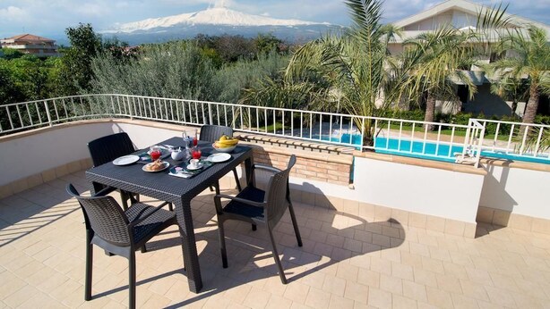 A terrace with a table set for dining, overlooking a swimming pool and a mountain in the background. - Villa Galati Resort (Mascali)