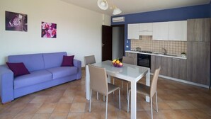 A modern living room with a sofa and a dining table with chairs. There is a kitchen area with cabinets and a stove. - Villa Galati Resort (Mascali)