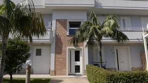 A modern two-story building with a balcony, a brick entrance, and a well-maintained garden with palm trees and a hedge. - Villa Galati Resort (Mascali)