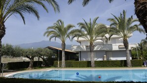 A pool surrounded by palm trees and a building with balconies. - Villa Galati Resort (Mascali)