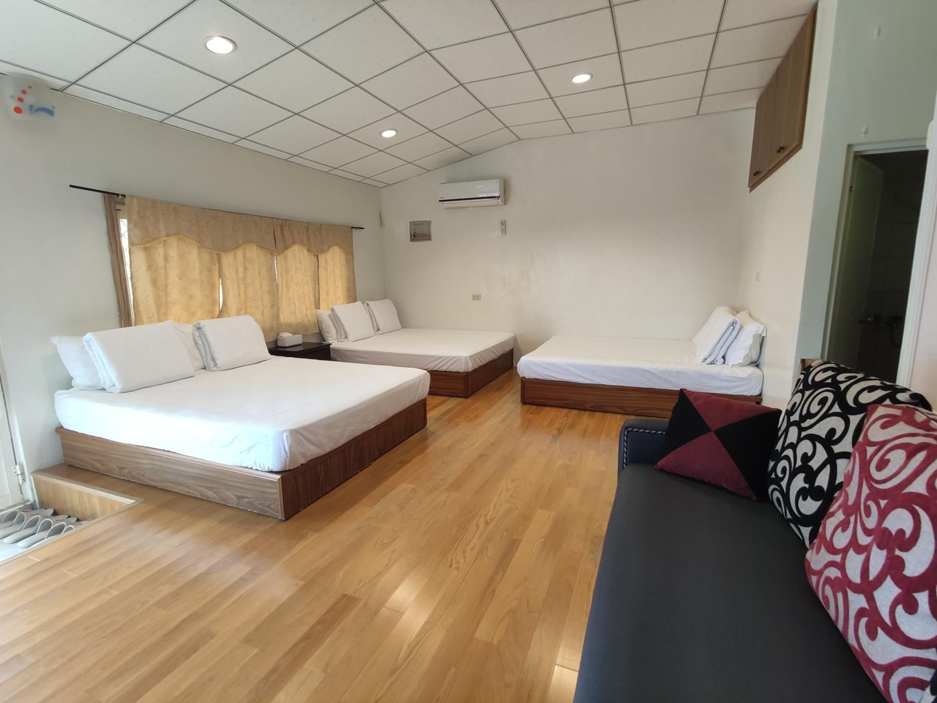 A hotel room with two beds, a sofa, and a wooden floor.