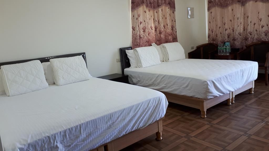 Zwei Einzelbetten mit Holzrahmen und weißer Bettwäsche in einem Zimmer mit Holzboden und einem floralen Vorhang.