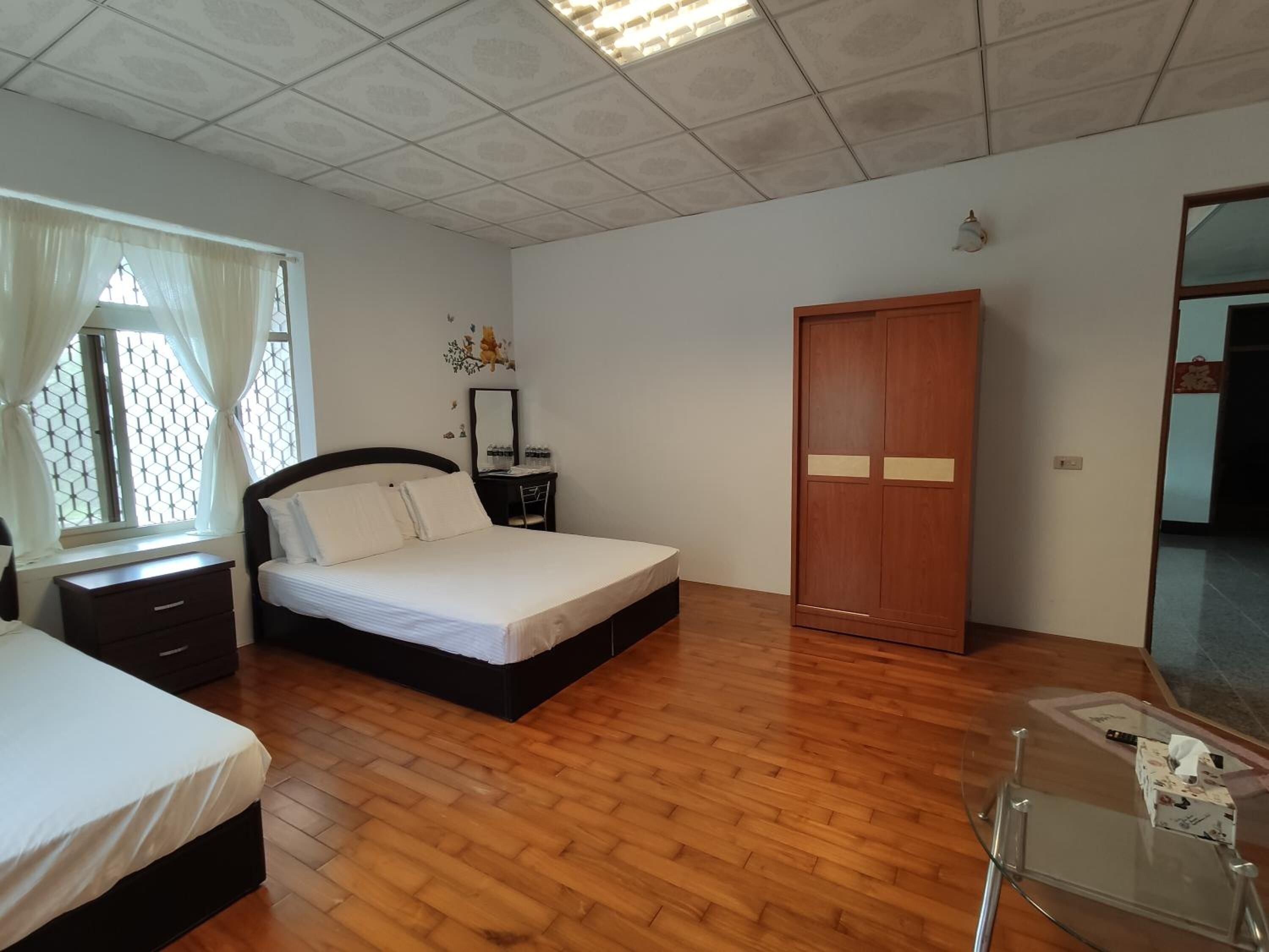 A bedroom with a bed, a nightstand, a dresser, a wardrobe, and a desk with a mirror.