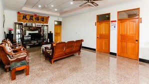 Eine Hotelhalle mit einem traditionellen Holzsofa, einem kleinen Holztisch und einem Deckenventilator. Holzdecken und ein Schild sind über dem Sofa angebracht.