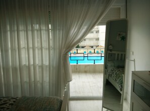 A bedroom with a view of a swimming pool, a bed, and a window with sheer curtains.