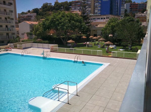 A swimming pool with a diving board and steps, surrounded by a fenced area with lounge chairs and umbrellas.