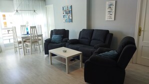 Una sala moderna con un sofá gris, una mesa de centro blanca y una zona de comedor con una mesa y sillas blancas.