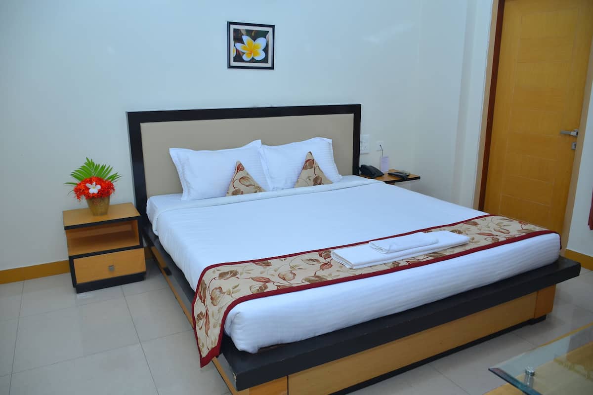 A neatly made bed with a floral bedspread, a bedside table with a plant, and a framed picture on the wall.