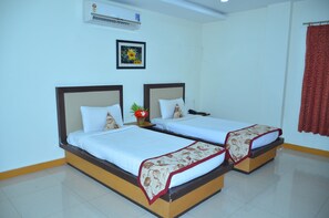 Habitación de hotel con dos camas individuales, aire acondicionado montado en la pared, un cuadro con flores enmarco y una cortina roja.