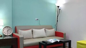 A living room with a sofa, a coffee table, a lamp, a clock, and a small yellow ottoman. - Chi Yu 85 (Ji'an)