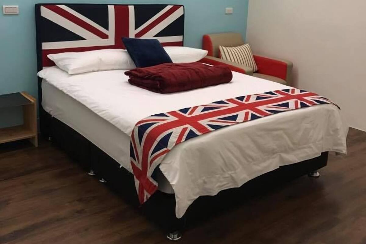 A bed with a Union Jack headboard, a white bedspread, and a red blanket.