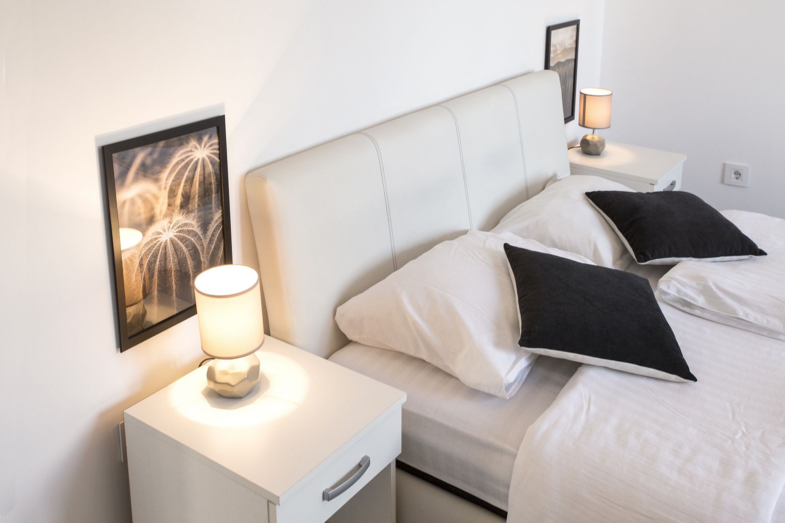 A neatly arranged hotel room with a bed, pillows, a bedside table with a lamp, and a framed picture on the wall.
