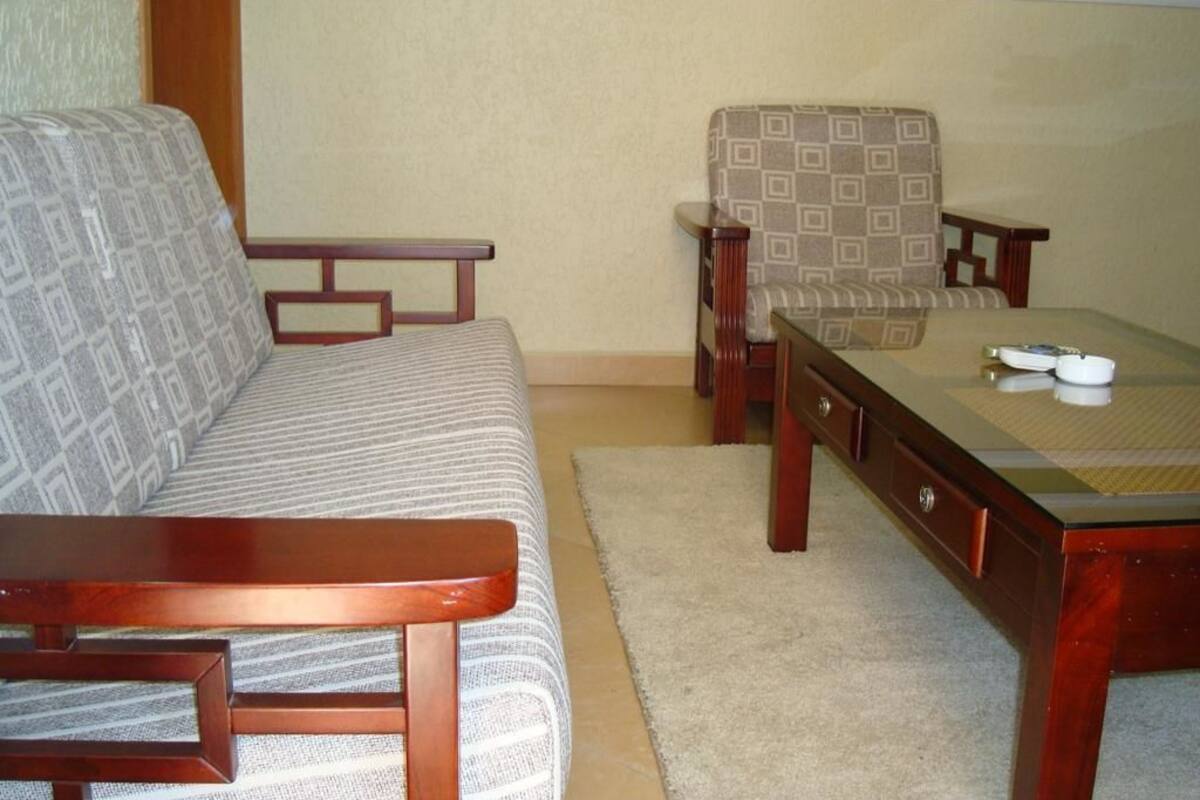 Uma sala de estar com sofá, uma poltrona estampada, mesa de centro de madeira e uma mesinha lateral.