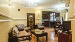 A living room with sofas, a coffee table, a TV, and a kitchen in the background. - Abla Apartment (Dar es Salaam)