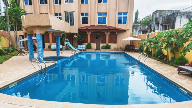 A swimming pool with a slide, surrounded by a building with multiple windows and a tiled roof. - Abla Apartment (Dar es Salaam)