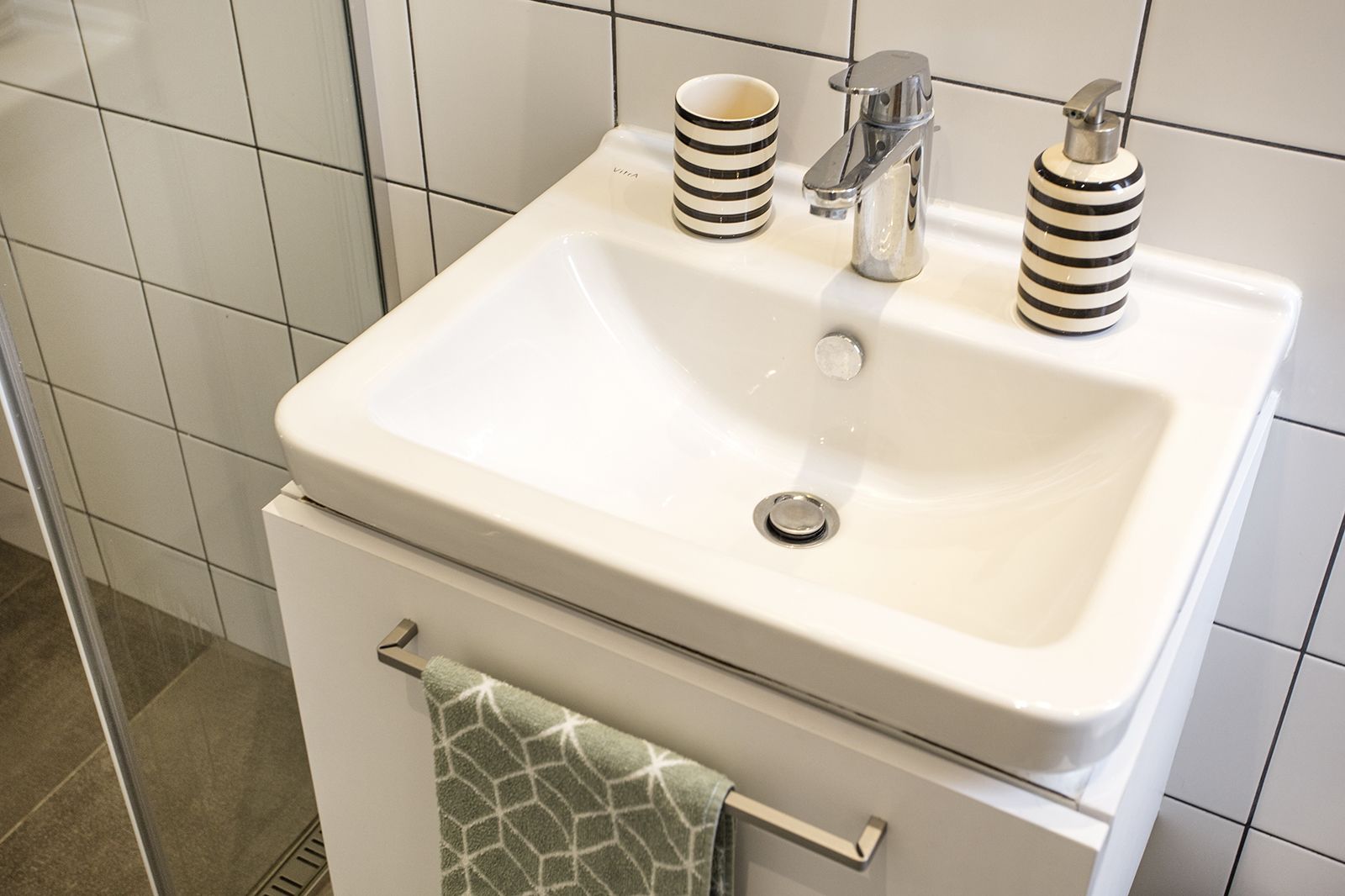 Een badkamer met een wit wastafel, twee gestreepte zeepdispensers, en een handdoek aan een metalen handdoekhouder.