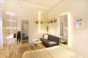 Una sala de estar moderna y bien iluminada con un sofá, una mesa de centro y un espejo grande. Se ve una zona de cocina al fondo.
