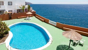 A swimming pool with a view of the sea, surrounded by a terrace with chairs and umbrellas.