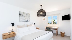 A modern bedroom with a large bed, a desk, and a window with a view.
