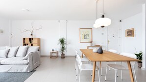 A modern living room with a sofa, dining table, chairs, a coffee table, a potted plant, and a framed picture on the wall.