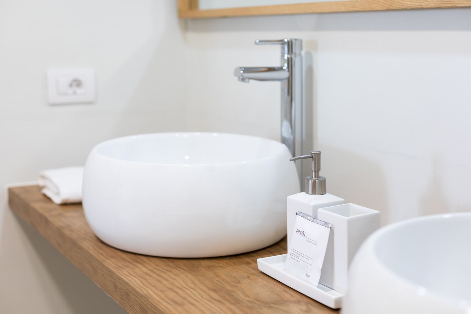 A modern bathroom with a white vessel sink, a chrome faucet, and a soap dispenser on a wooden shelf.