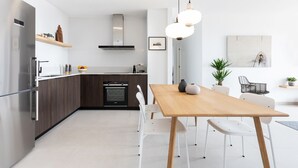 A modern kitchen with a wooden dining table, white chairs, and a pendant light.