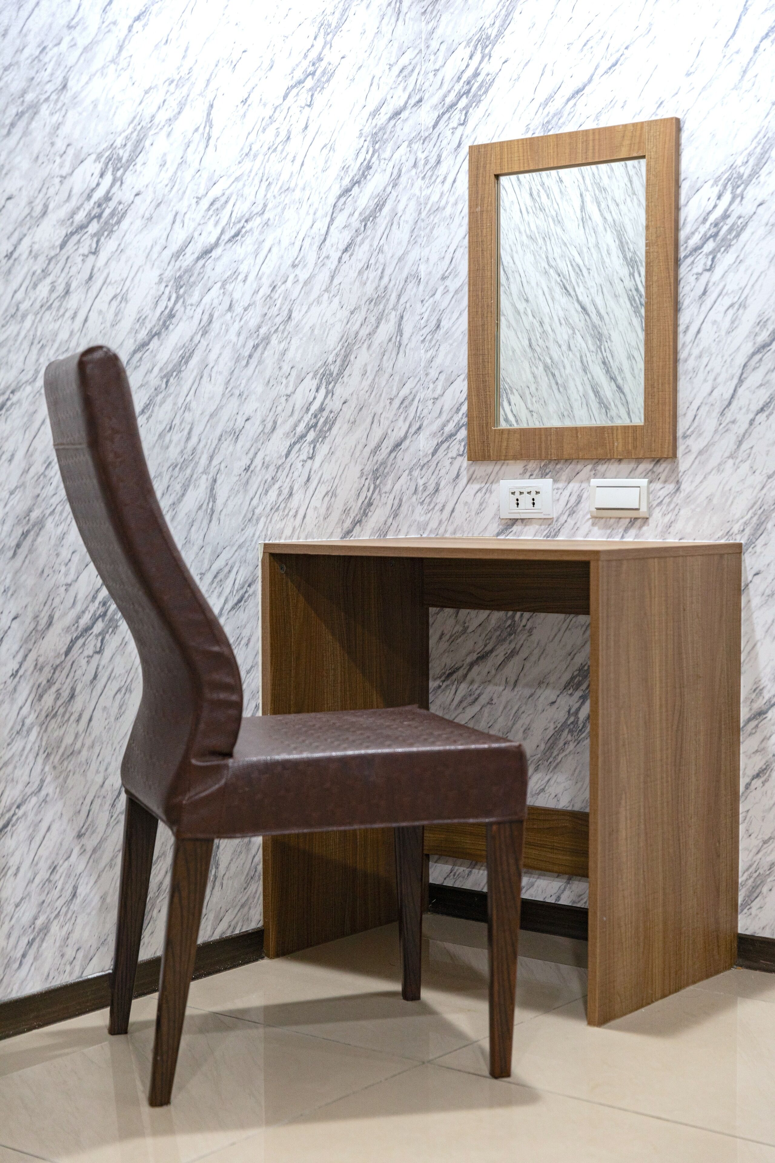 A corner desk with a chair, a mirror, and a marble wall.